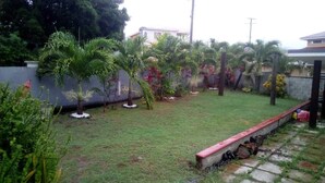 A residential garden with a well-maintained lawn, various tropical plants, and a stone pathway leading to a gated entrance. - Beausejour Vista Studio1 (Gros Islet)