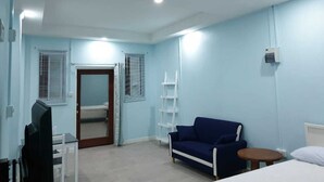 A room with a blue wall, a white ceiling fan, a white shelf, a blue sofa, a white bedside table, and a door with a mirror. - Beausejour Vista Studio1 (Gros Islet)