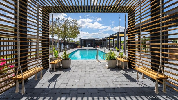Un área de piscina con paredes de listones de madera, plantas en macetas y un cielo azul despejado.