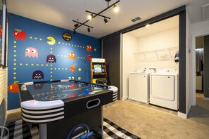 Um quarto com mesa de pebolim, máquina de fliperama do Pac-Man e máquina de lavar.