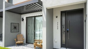 Entrada de un edificio moderno con una puerta oscura, un felpudo y dos sillas de madera.