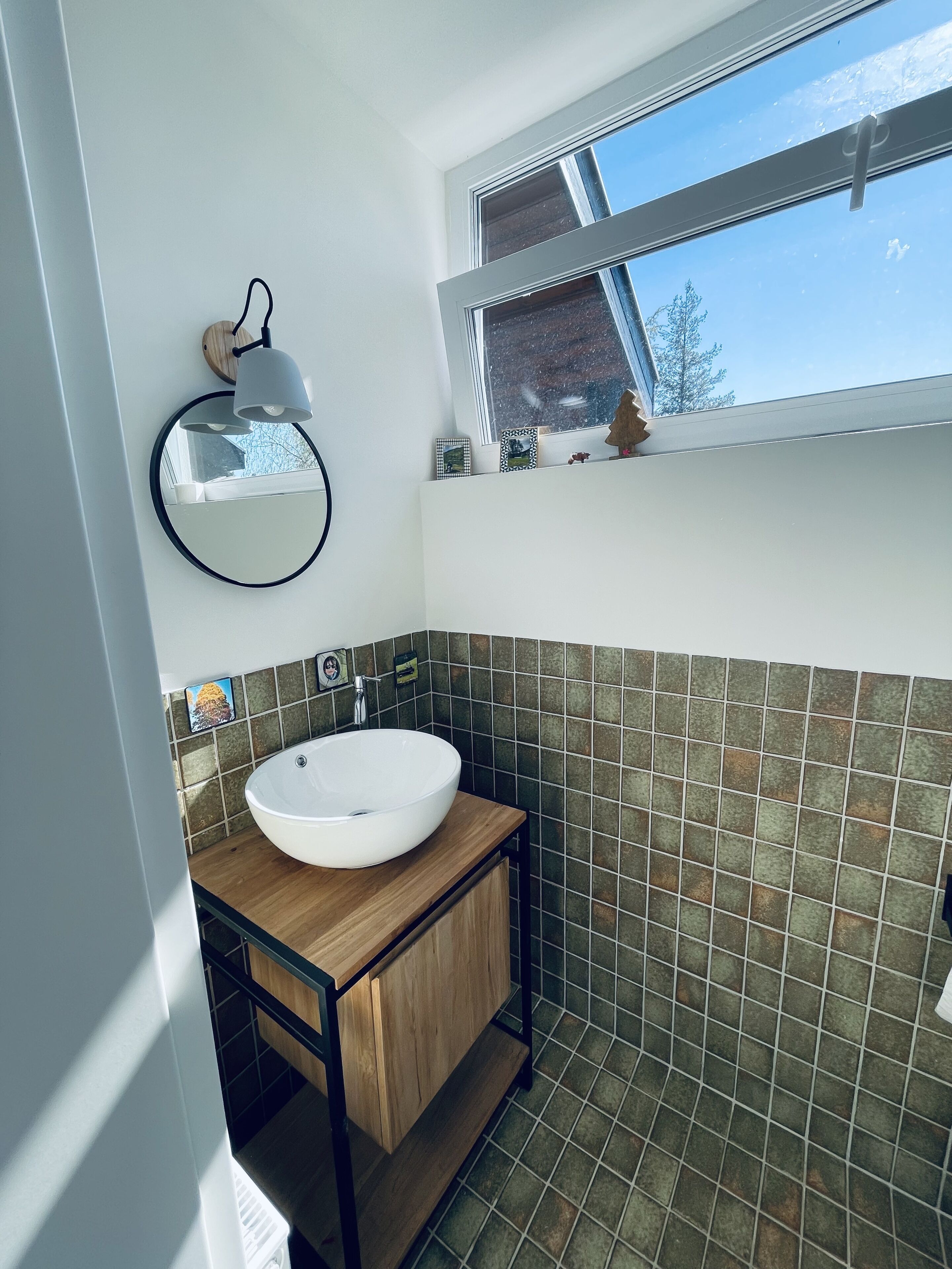 A bathroom with a white sink, a round mirror, and a window above the sink.