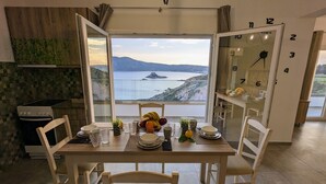 A dining area with a table set for four, a view of the sea and mountains, and a clock on the wall. - Cute Apartments (Κέφαλος)