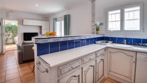 A modern kitchen with white cabinets, blue and white tiles, a large island with a sink, and a dining area with a sofa and table. - LES HUPPES: Nice ground floor house in l'Escala with air-conditioning and large terrace (L'Escala)