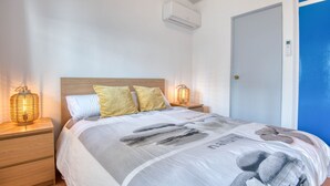 A bedroom with a bed, two bedside lamps, a nightstand, a door, and an air conditioning unit. - LES HUPPES: Nice ground floor house in l'Escala with air-conditioning and large terrace (L'Escala)
