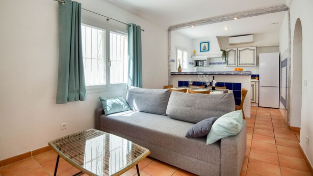 A compact living space with a sofa, a glass-top table, and a kitchen area with a microwave, refrigerator, and tiled backsplash. - LES HUPPES: Nice ground floor house in l'Escala with air-conditioning and large terrace (L'Escala)