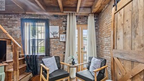 Interior rústico de una cabaña con dos sillones de cuero, una mesa de madera, un televisor y una escalera que lleva a una puerta.