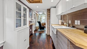 Una cocina moderna con armarios blancos, encimera de madera y pared decorativa de ladrillo.