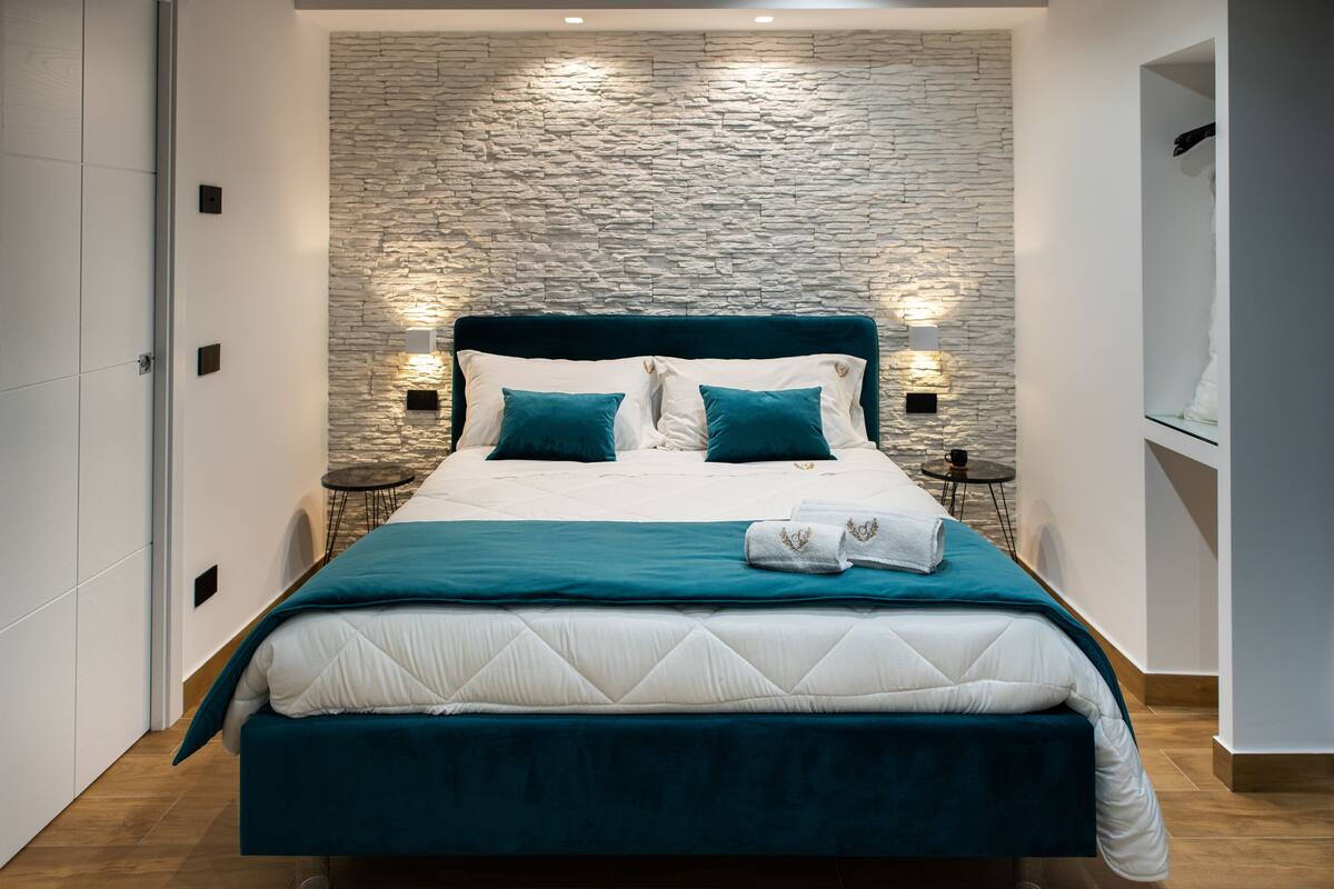 Ein modernes Schlafzimmer mit Steinwand, einem großen Bett mit türkisfarbenen Bettwäsche und zwei Nachttischen mit Lampen.