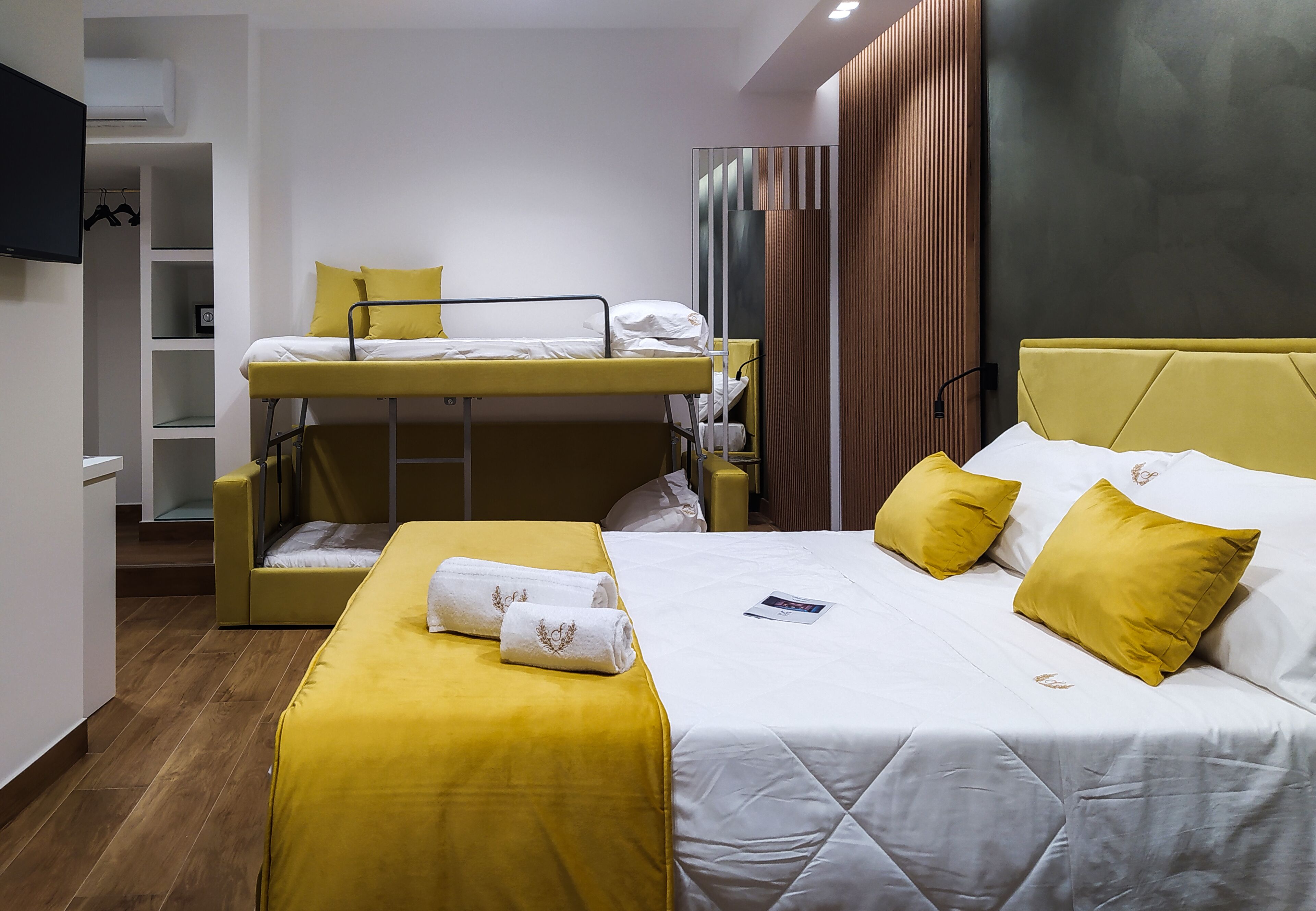 A hotel room with a bunk bed, a single bed, and a desk.