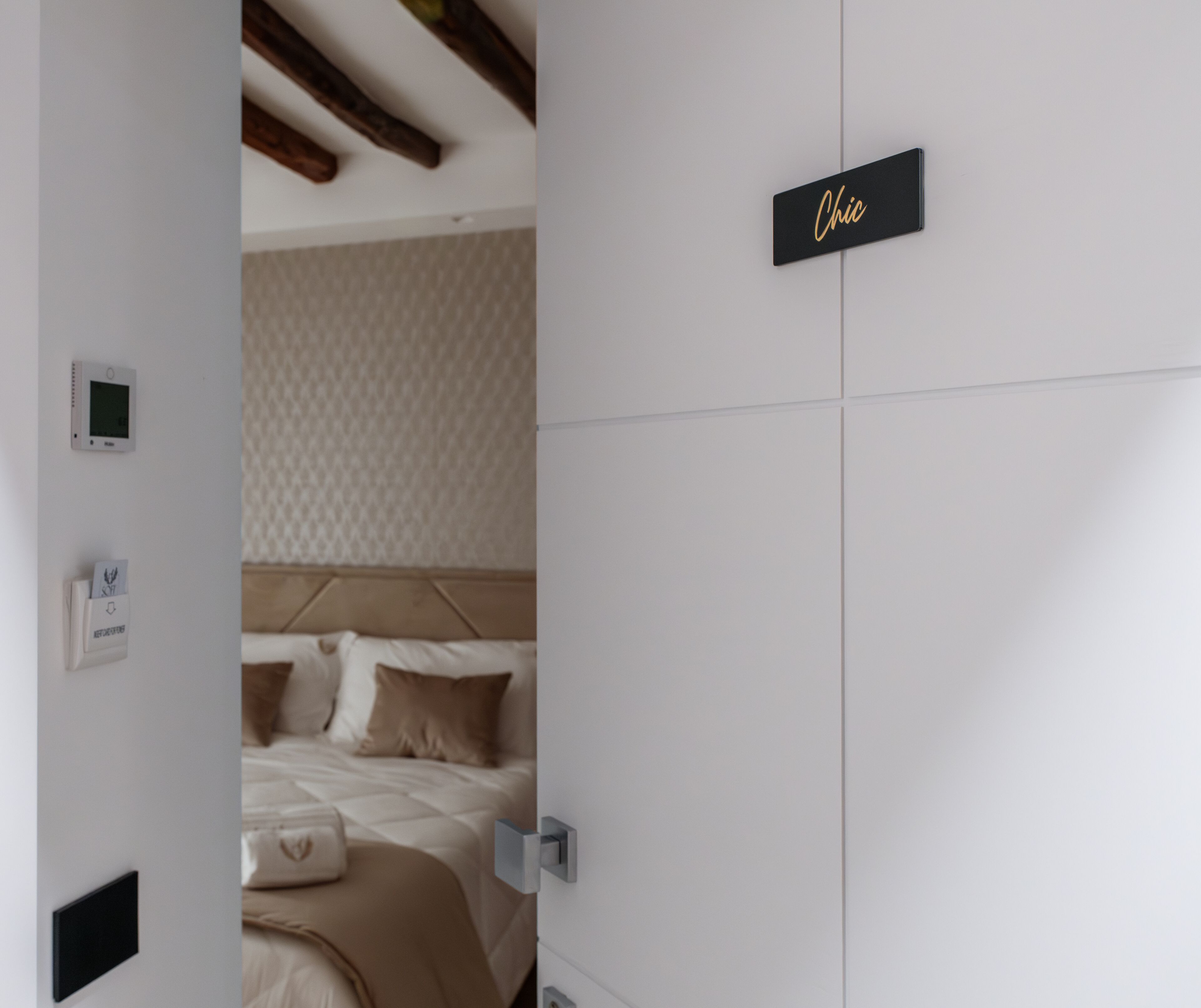 Una habitación de hotel con cama, termostato, panel de control del termostato, mesita de noche y una puerta con un cartel que dice 'Chic'.