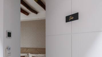 Una habitación de hotel con cama, termostato, panel de control del termostato, mesita de noche y una puerta con un cartel que dice 'Chic'.