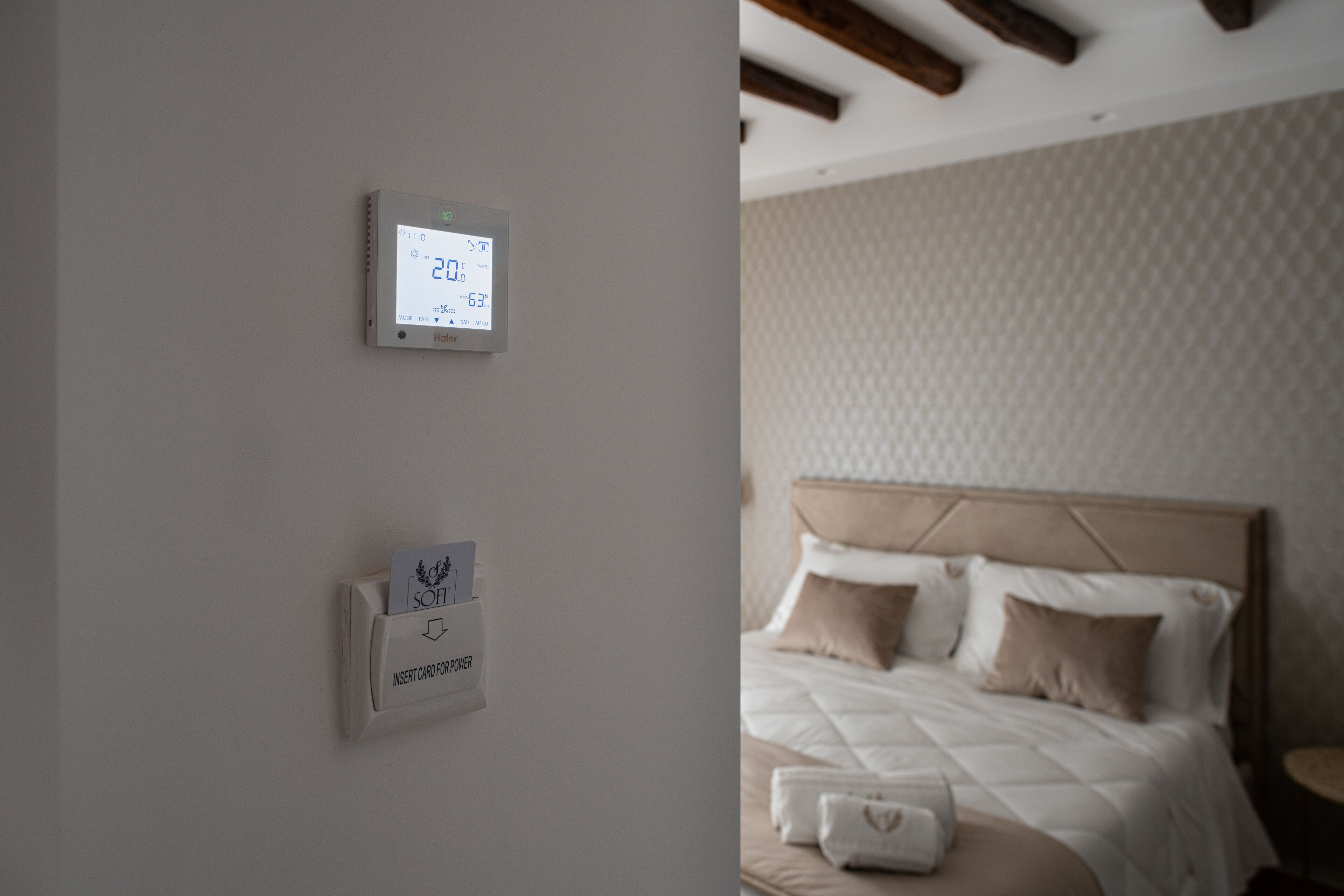 Ein Thermostat und ein Kartenlesegerät an einer Wand, sowie ein Bett mit Kissen und Decke.