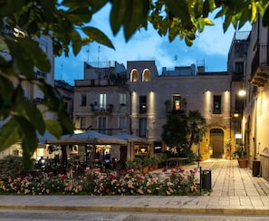 A courtyard with outdoor seating, a flower garden, and buildings with balconies and lights. - Sofi' Center Rooms (Sciacca)