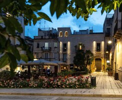 Un cortile con posti a sedere all'aperto, un giardino fiorito e edifici con balconi e luci.
