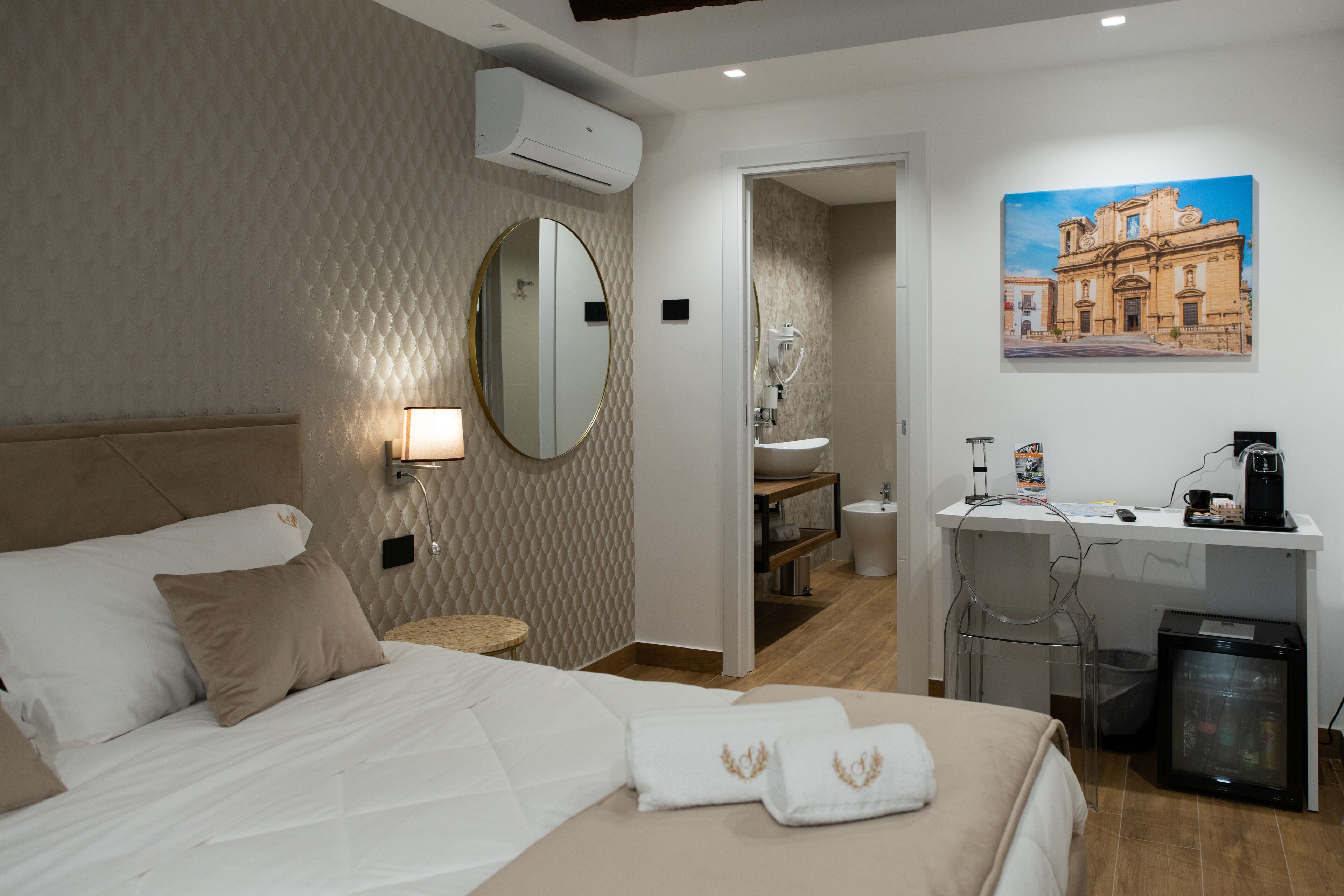 Una habitació d'hotel amb un llit, una escriptori amb un banypet, un mirall i un quadre a la paret.