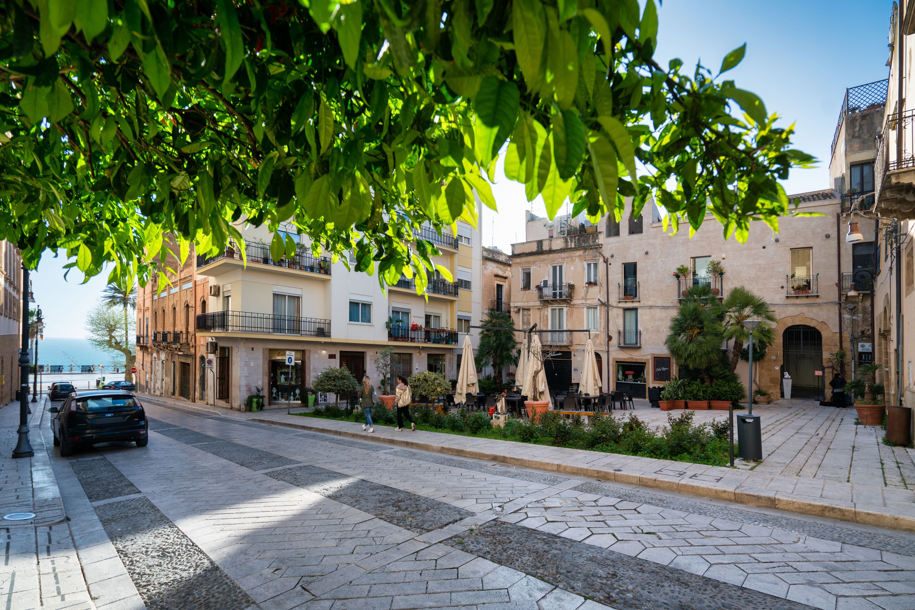 A street with buildings, a car, and a pedestrian.