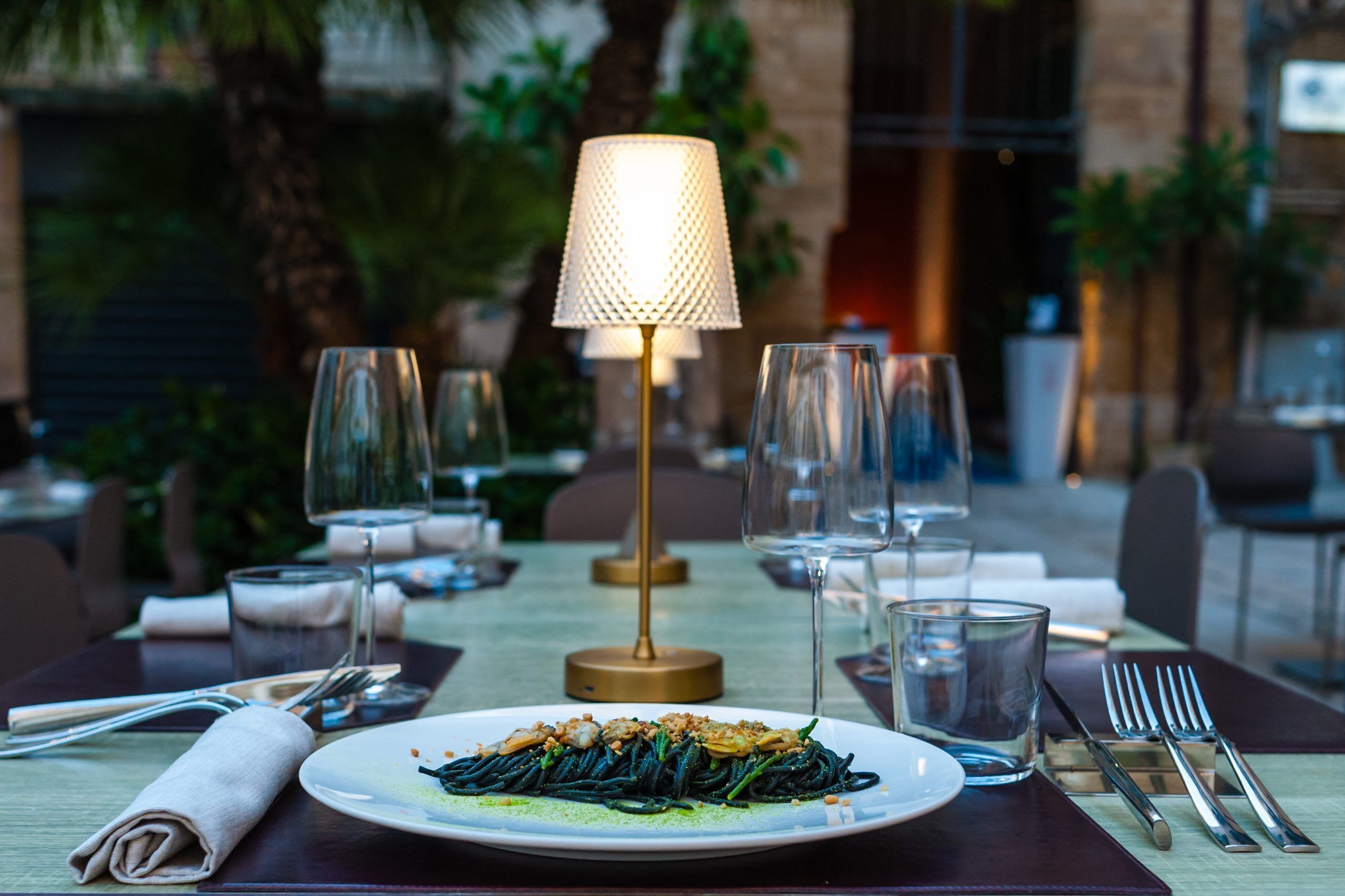 A dining table set with a plate of pasta, wine glasses, and cutlery.