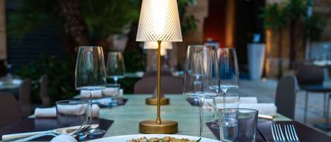 A dining table set with a plate of pasta, wine glasses, and cutlery.