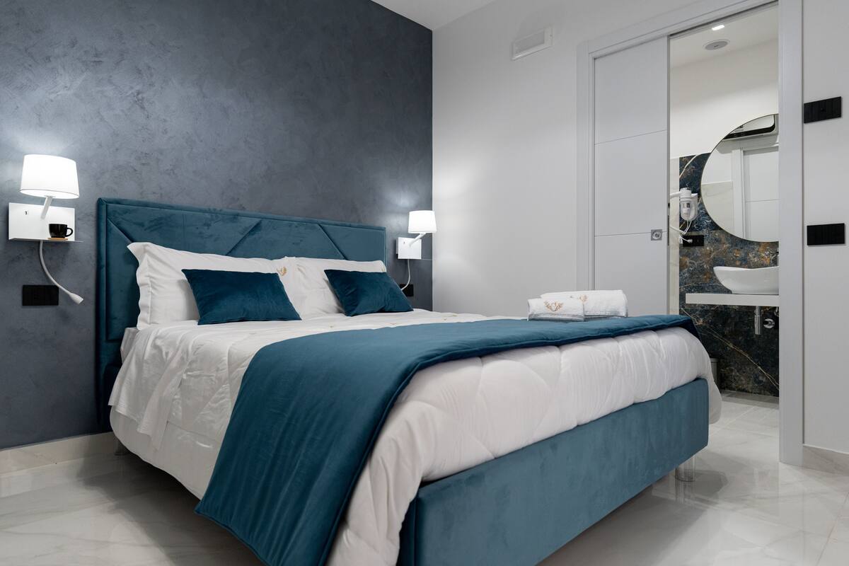 Ein modernes Schlafzimmer mit einem großen Bett, zwei Nachttischlampen, einem Nachttisch und einem durch eine offene Tür einsehbaren Badezimmer.