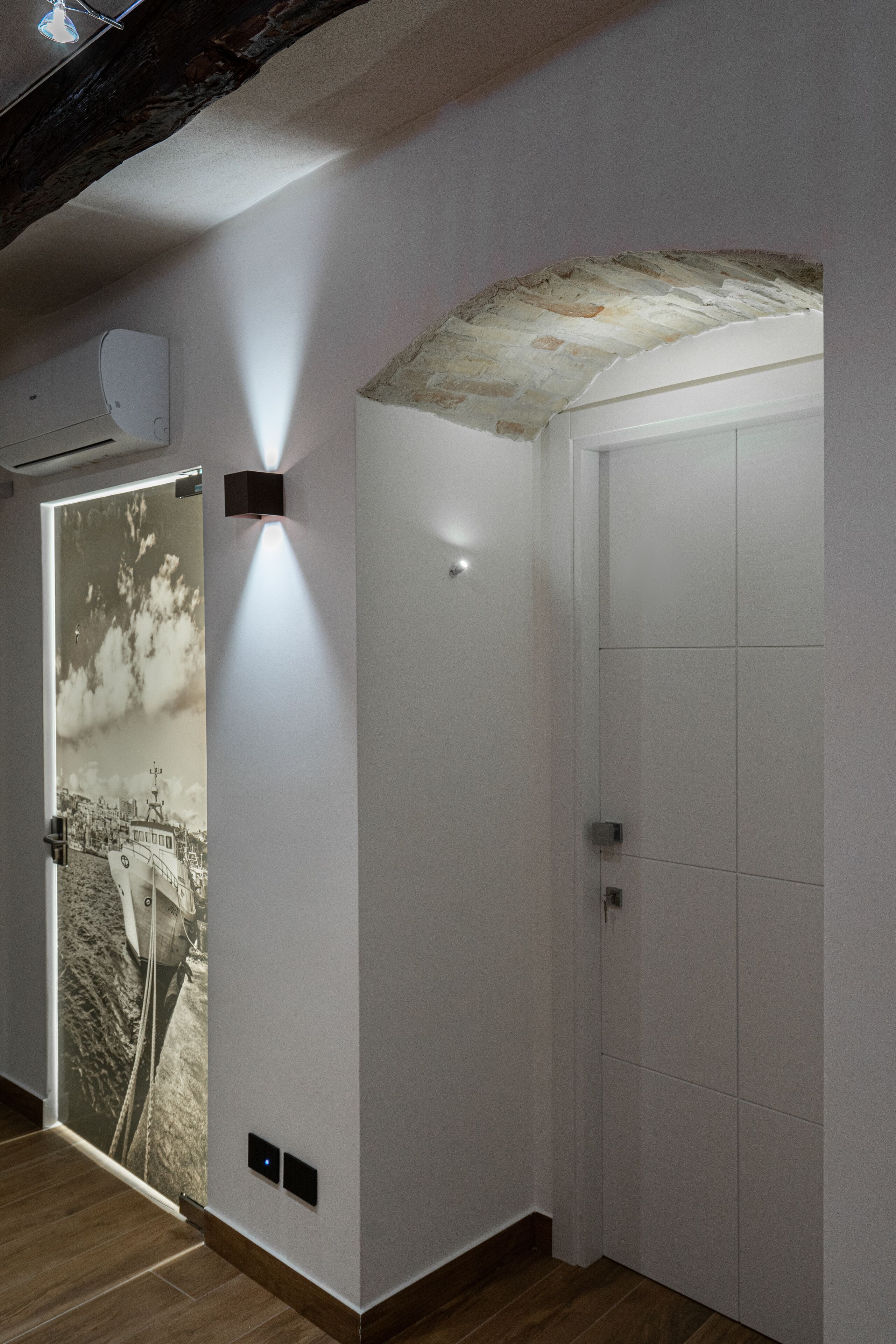 A hallway with a white door, a wall-mounted light, and a door with a black and white photograph.