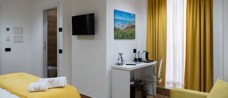 A hotel room with a bed, a desk, a chair, a TV, and a window with curtains.