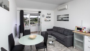 A modern living room with a glass dining table, a grey sofa, and a microwave on a wooden counter. - Apartment Mia - Two Bedroom Apartment with Balcony (Split)