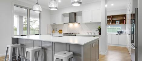 A modern kitchen with a large island, white cabinetry, and pendant lighting.