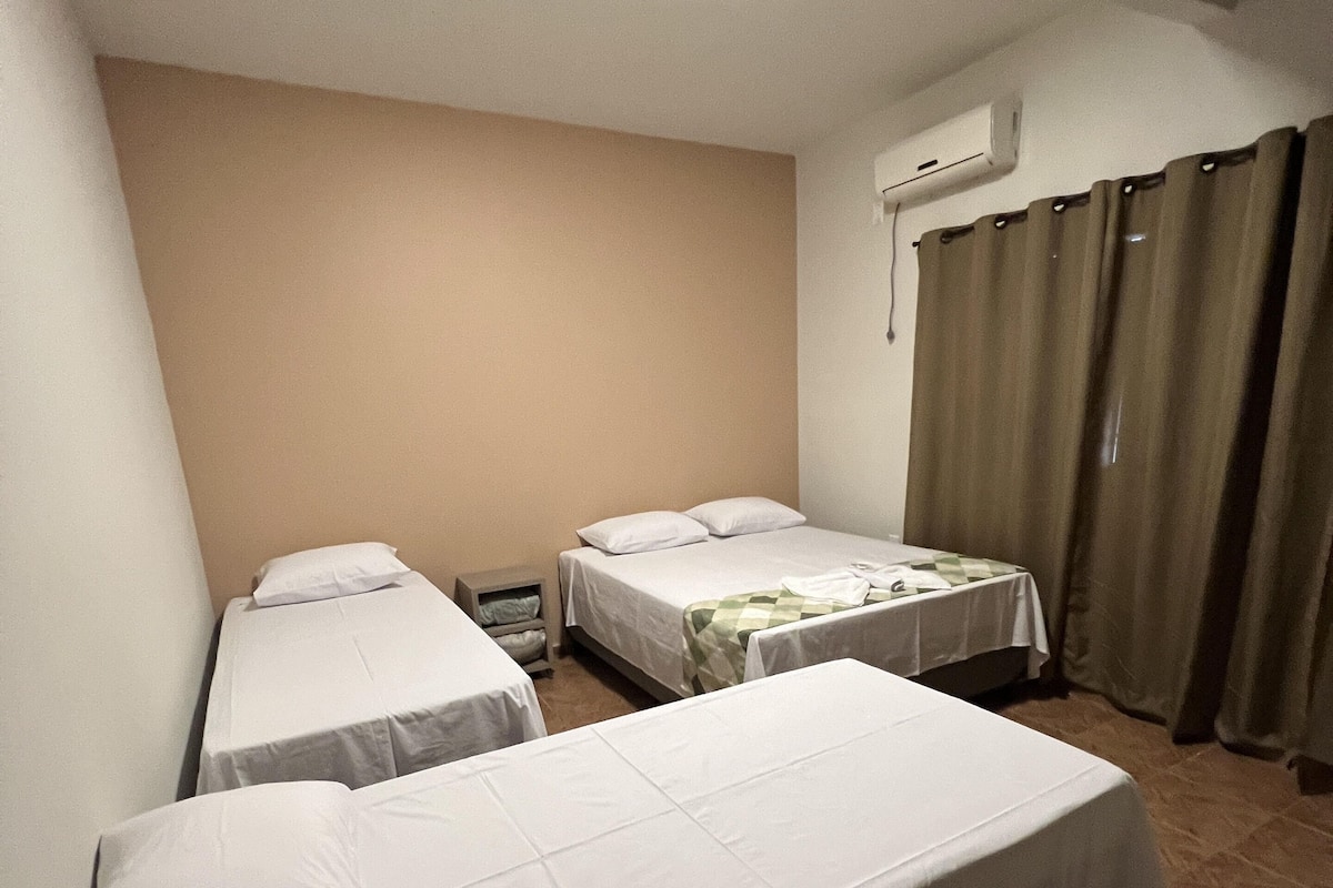 Een hotelkamer met twee enkele bedden, een tafeltje, een stoel, een nachtkastje en een raam met gordijnen.