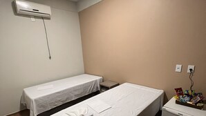 Quarto de hotel pequeno com duas camas de solteiro, um minibar e um aparelho de ar condicionado na parede.