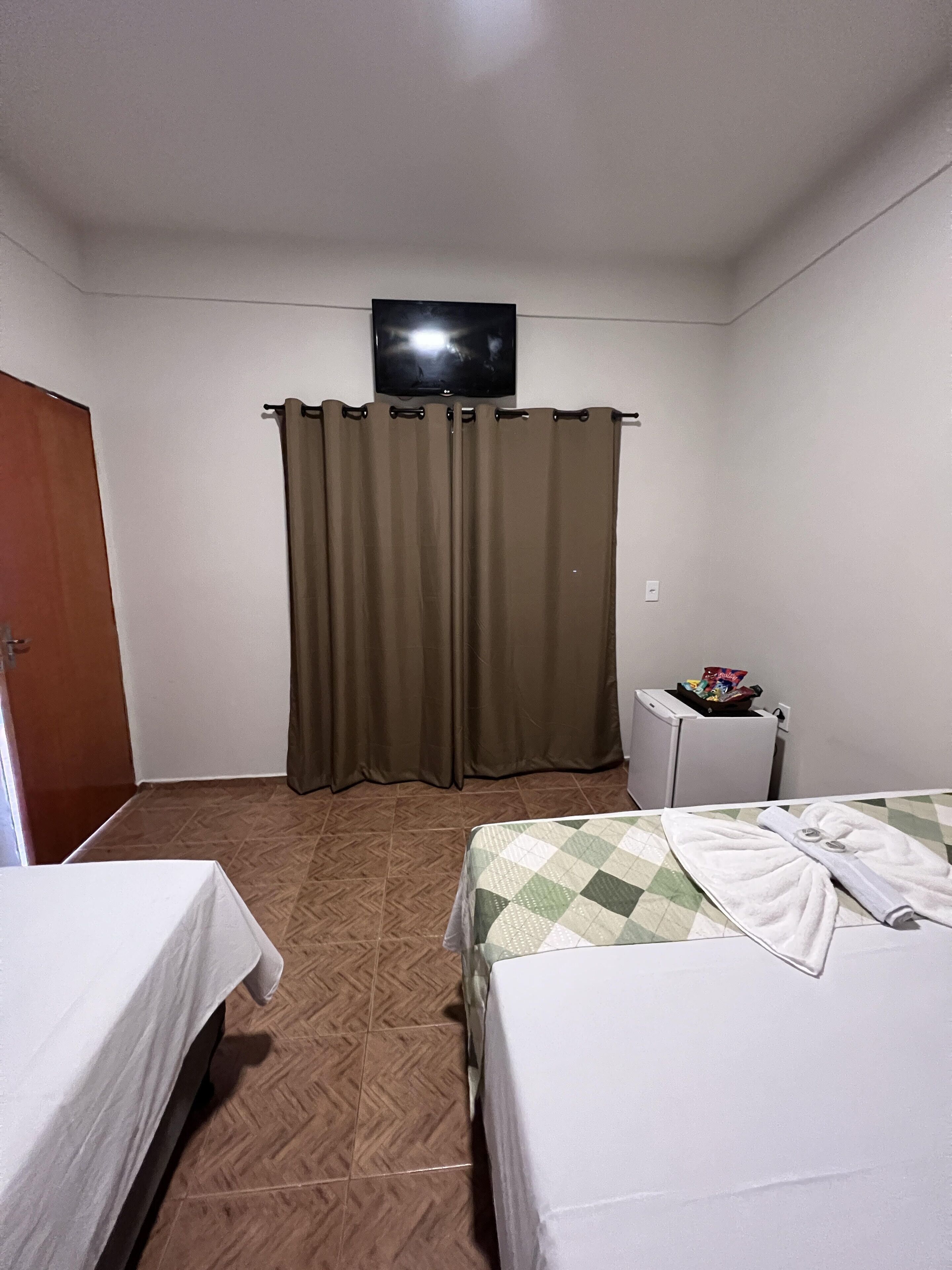 A hotel room with two beds, a television mounted on the wall, a small table with snacks, and a door.