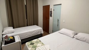 Quarto de hotel com duas camas, uma mesa pequena, um refrigerador e uma porta com uma placa.