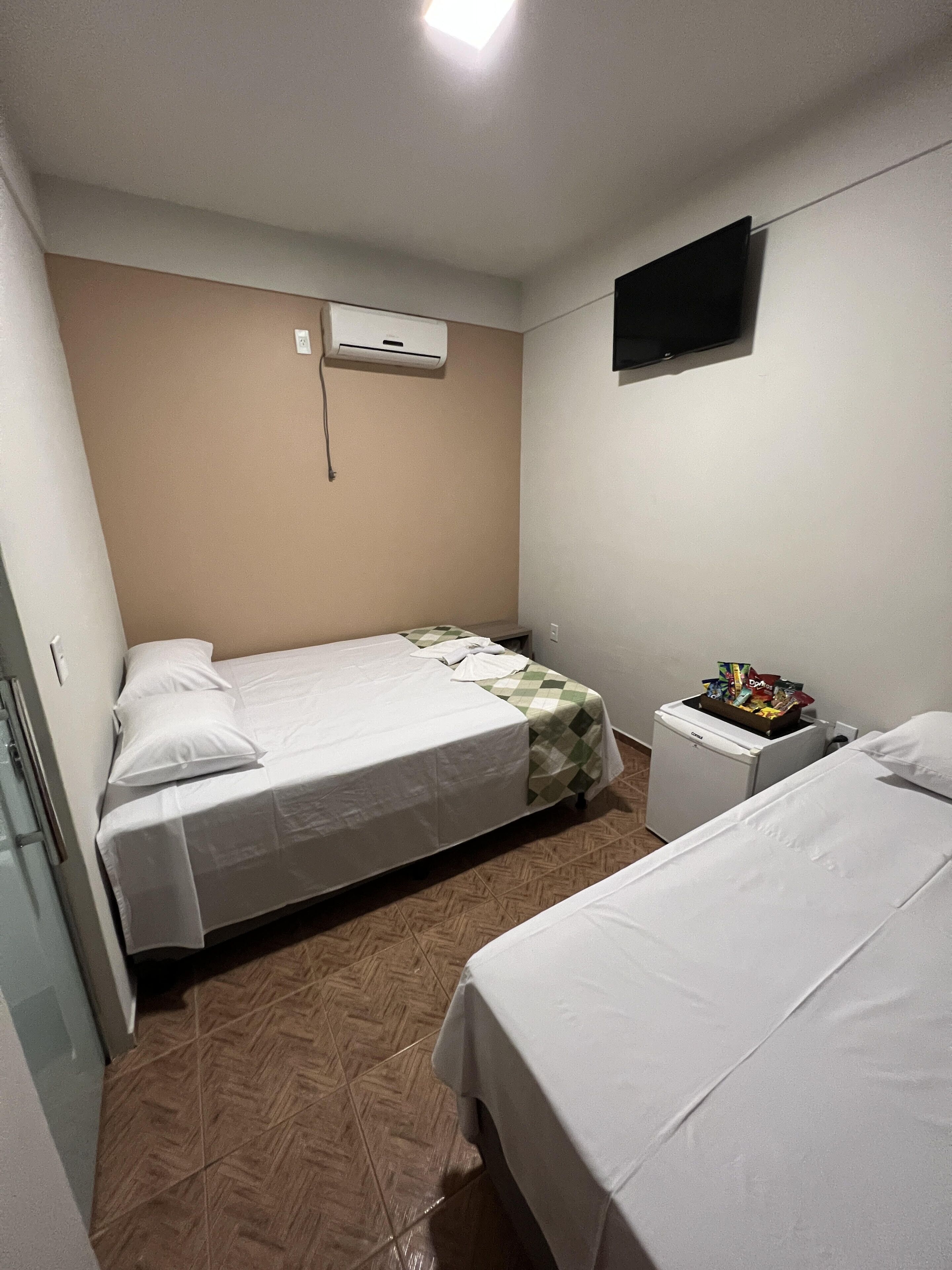 A small, clean room with two beds, a small table, a TV, and a heater.