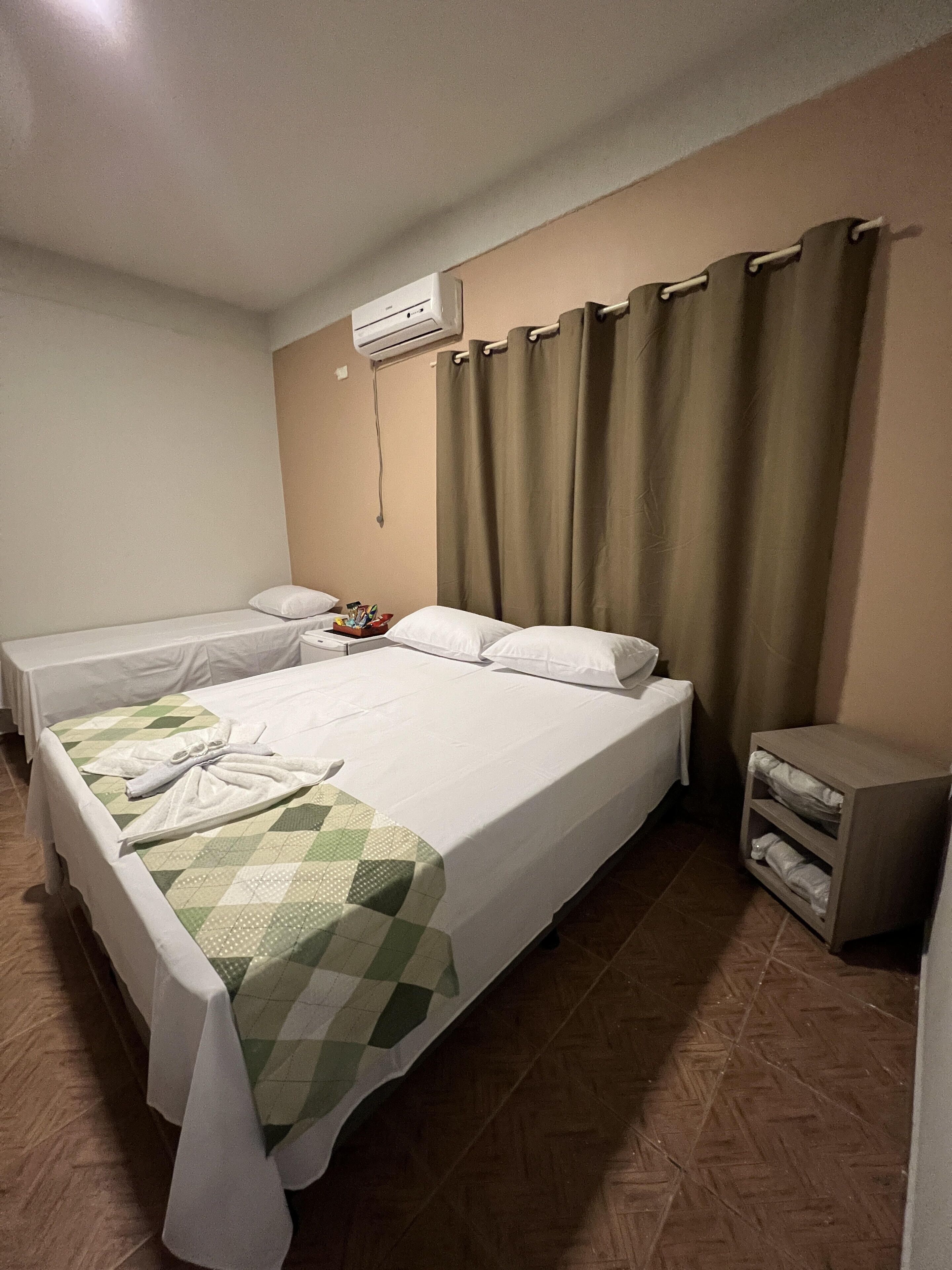 Ein Hotelzimmer mit einem großen Bett, einem Nachttisch, einer kleinen Kommode und einer Klimaanlage an der Wand.