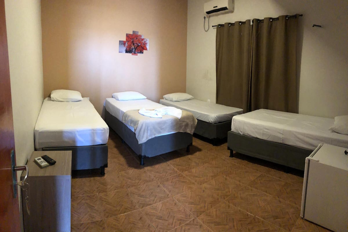 Een kamer met drie eenpersoonsbedden, een klein tafeltje met een afstandsbediening en een koelkast.