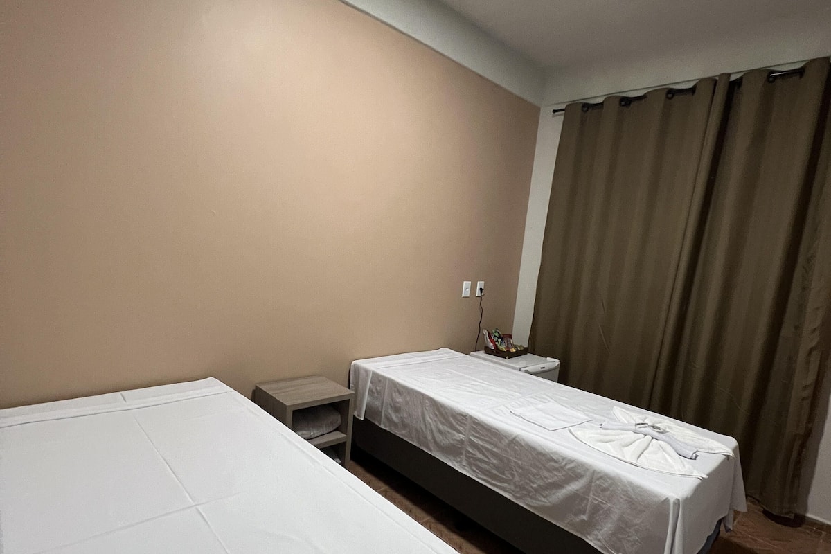 Een hotelkamer met twee bedden, een nachtkastje, een lamp en een gordijn.