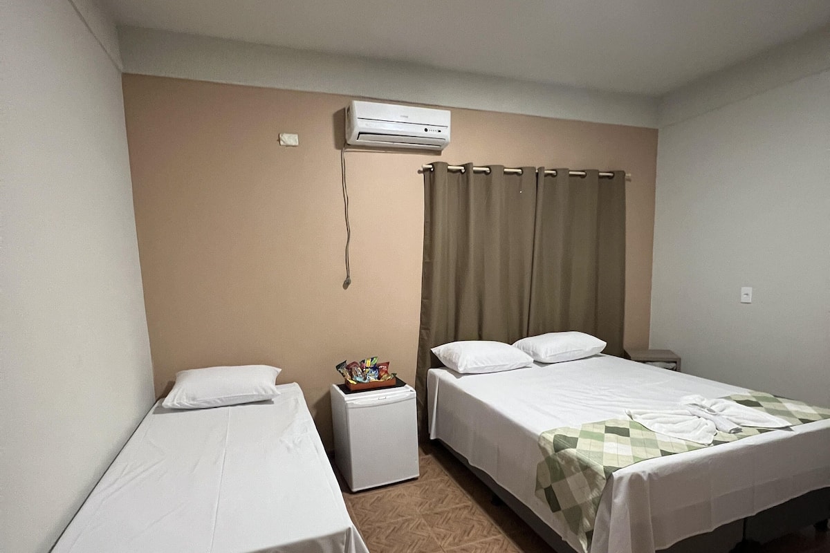 Een hotelkamer met twee enkele bedden, een klein nachtkastje met een lamp, een airconditioner en een gordijn.