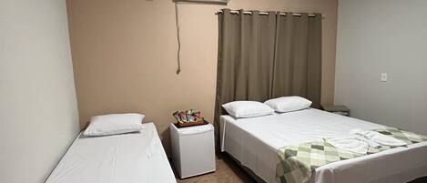 A hotel room with two single beds, a small bedside table with a lamp, an air conditioning unit, and a curtain.