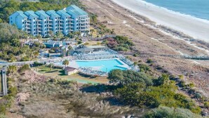 Un complexe hôtelier doté d’une grande piscine, offrant une vue sur la plage et comprenant plusieurs bâtiments.