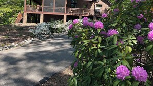 A two-story wooden cabin with a balcony, surrounded by lush greenery and flowering plants. - Beautiful Mountain View with Large Saltwater Pool (Landrum)