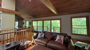 A spacious living room with a wooden ceiling, large windows, a brown leather sofa, and a glass coffee table. - Beautiful Mountain View with Large Saltwater Pool (Landrum)
