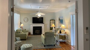 A living room with a fireplace, a television, and a ceiling fan.