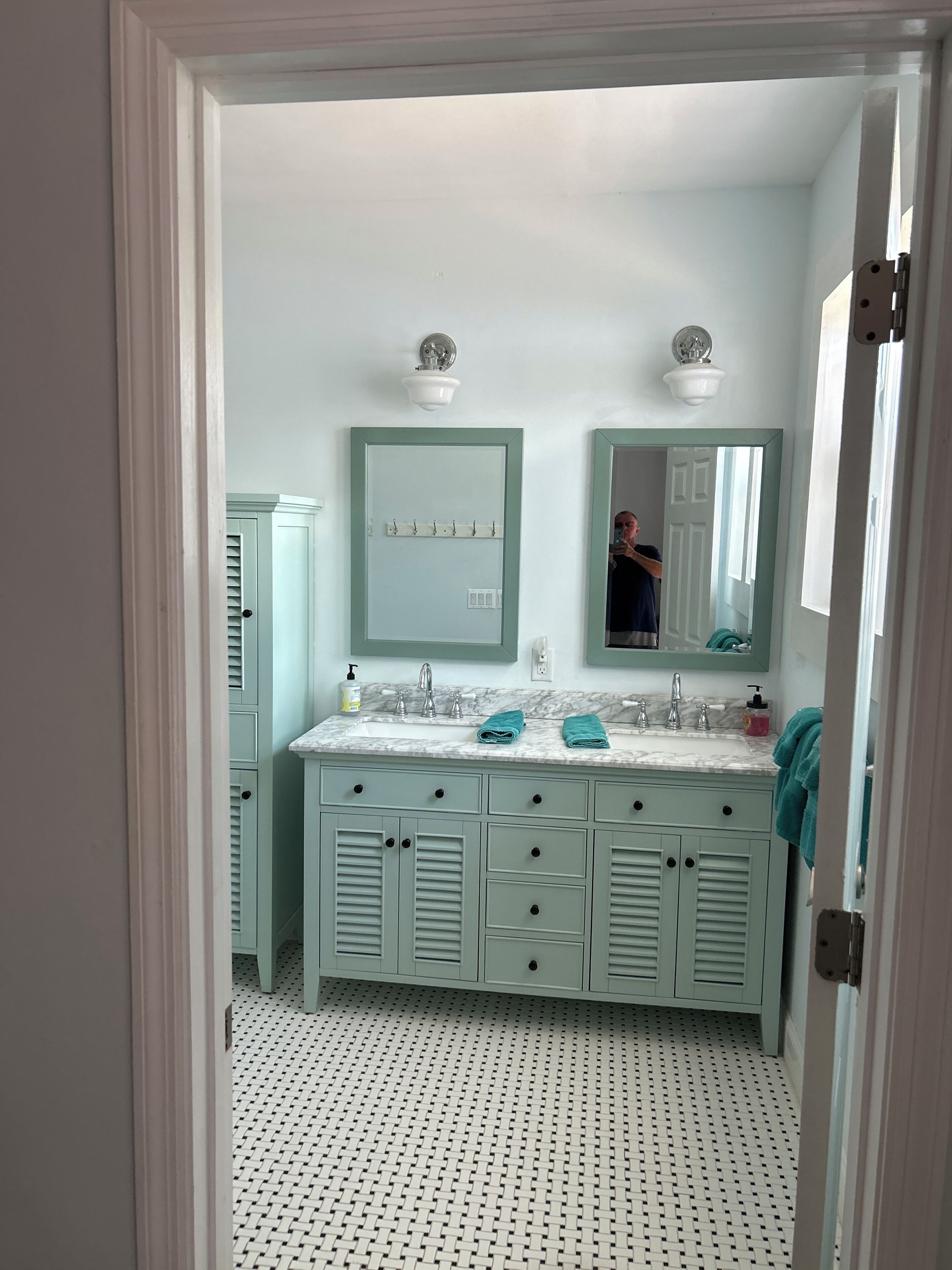 A bathroom with a white tiled floor, a sink with a marble countertop, and a mirror above it.