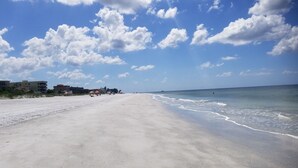 Una playa con cielo despejado y algunas nubes. Se ven edificios y sombrillas a lo largo de la orilla.