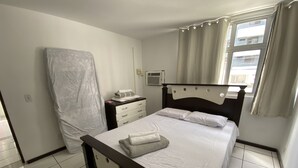 A bedroom with a bed, a nightstand, a window with curtains, and a wall-mounted air conditioning unit. - 3 quartos a 2 quadras da Praia (Maceió)