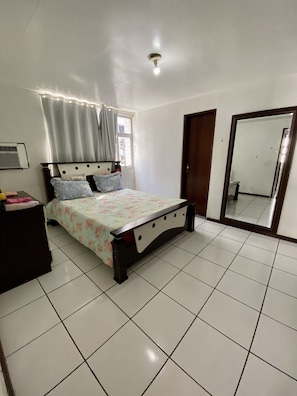 Quarto com cama, penteadeira, espelho e janela com cortinas.