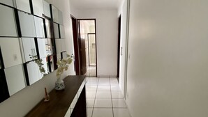 A hallway with a long wooden bench, a tiled floor, and a wall with a mirror and decorative items. - 3 quartos a 2 quadras da Praia (Maceió)