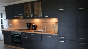 A modern kitchen with dark cabinets, a stainless steel sink, and a built-in oven. - Enjoy the Thuringian Forest in the barrier-free vacation home "Bergwiese" (Neuhaus am Rennweg)