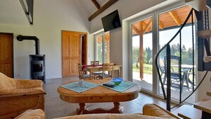 A cozy living room with a fireplace, wooden furniture, and large windows offering a view of the outdoors. - Enjoy the Thuringian Forest in the barrier-free vacation home "Bergwiese" (Neuhaus am Rennweg)