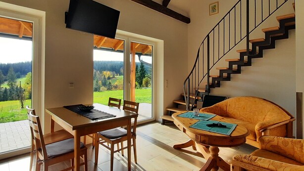A dining area with a wooden table and chairs, a sofa, and a staircase leading to an upper floor. - Enjoy the Thuringian Forest in the barrier-free vacation home "Bergwiese" (Neuhaus am Rennweg)